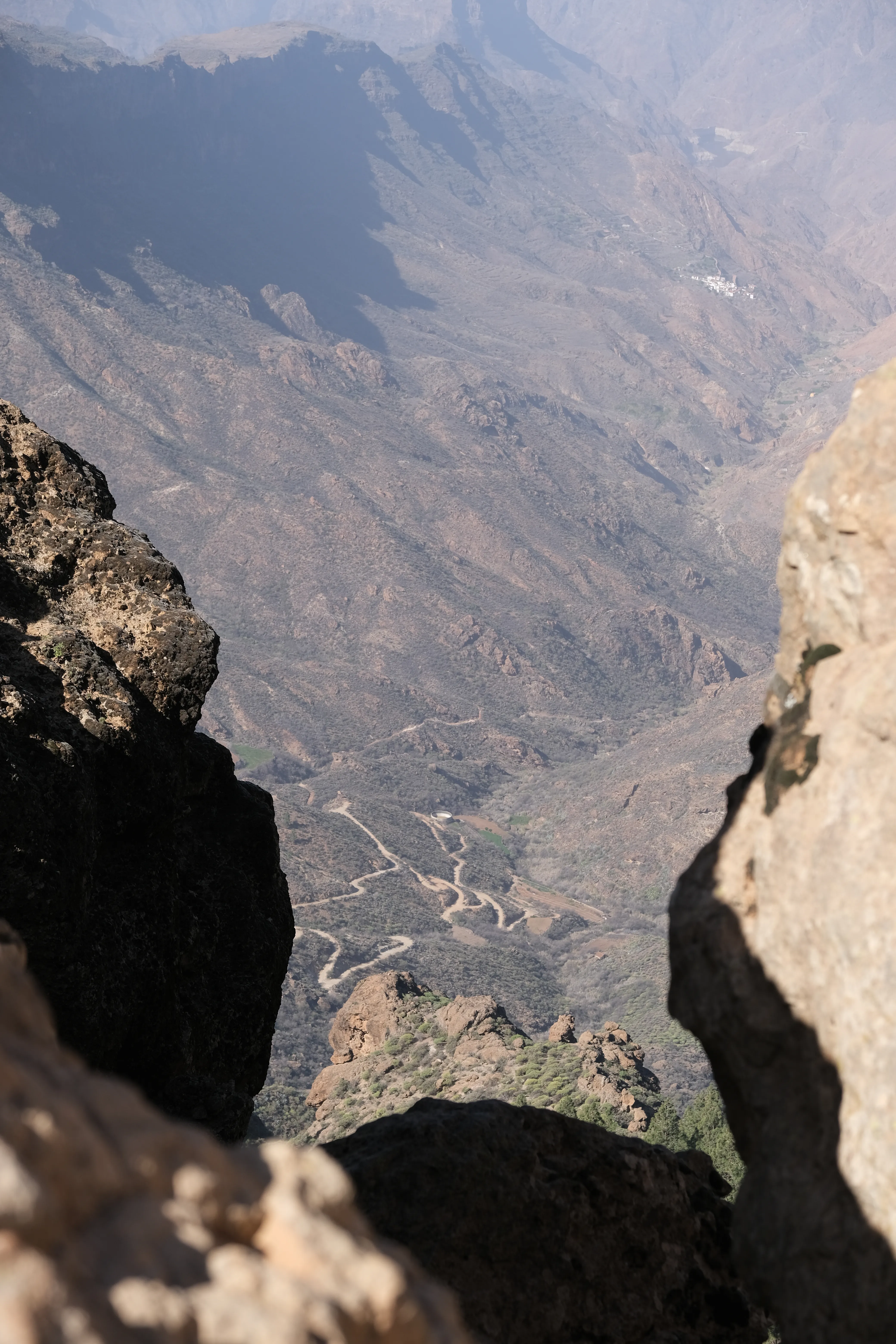 Rocks frame the view into a deep valley. A road meanders through the arid landscape far below.