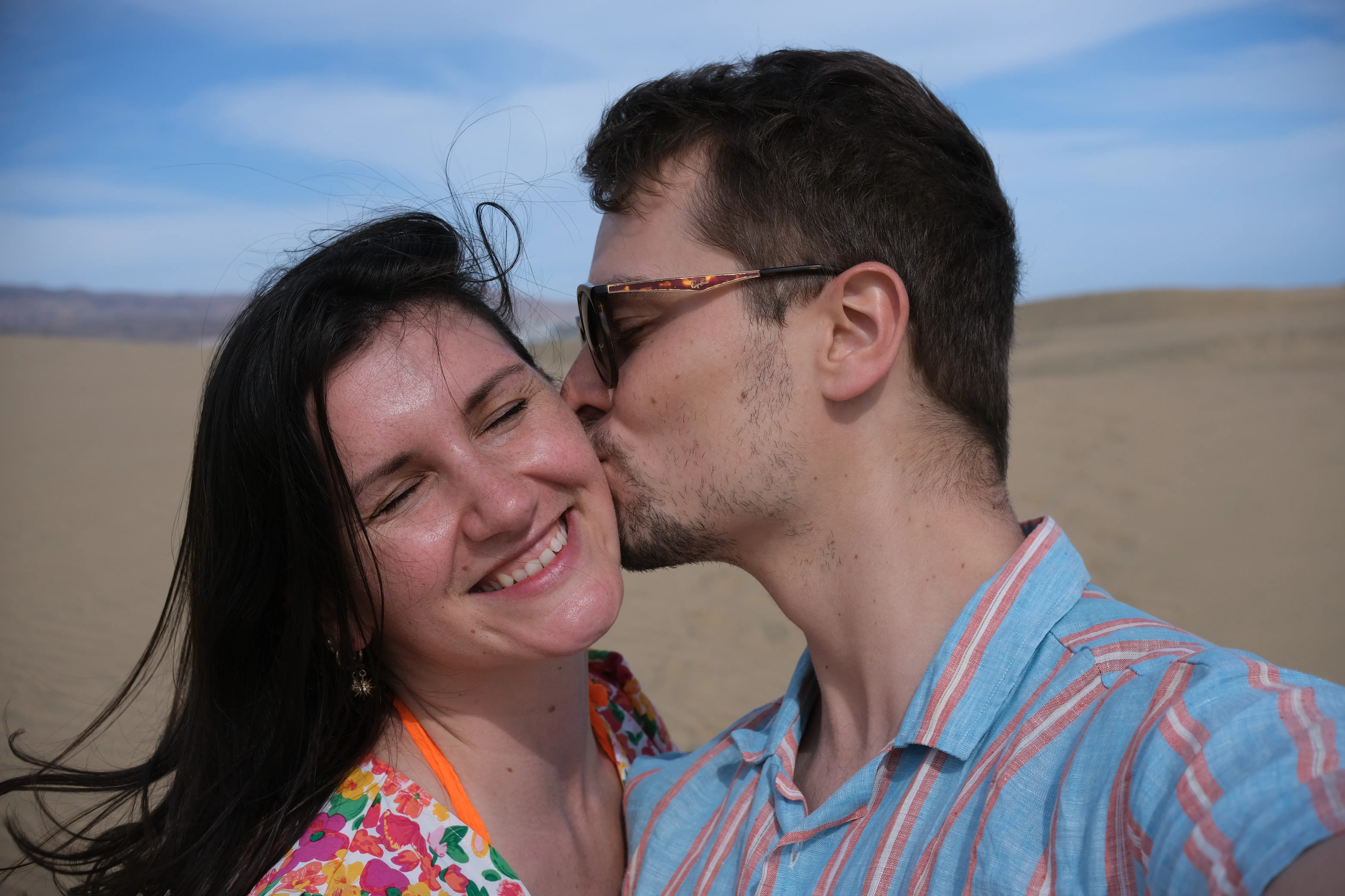 Portrait of Connor kissing Jillian on the cheek in the dunes of Maspalomas.