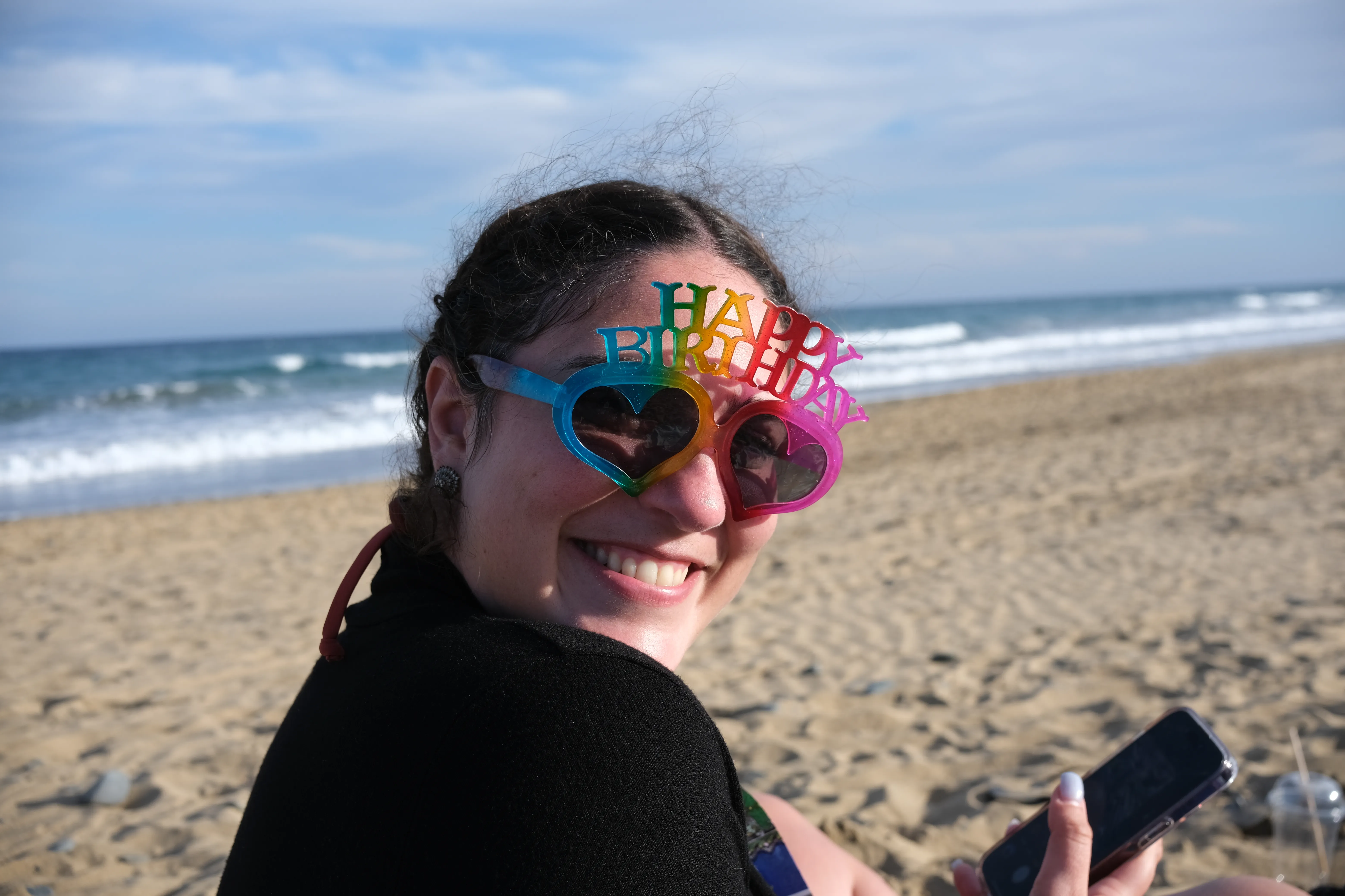 Portrait of Alessandra at the beach wearing colorful sunglasses with "Happy birthday" written across the top.