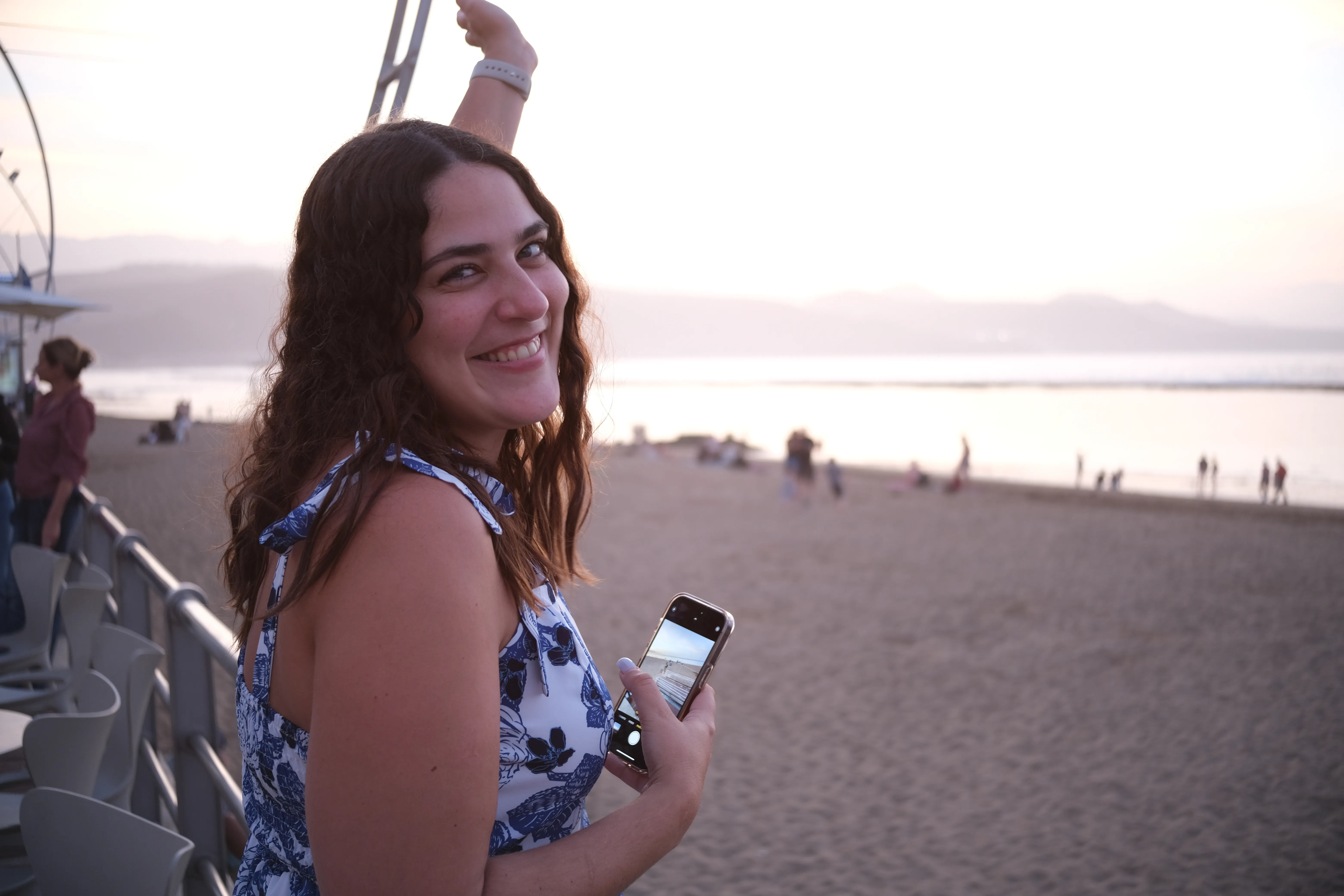 Alessandra poses in front of the sunset over the beach wearing a white and blue dress.